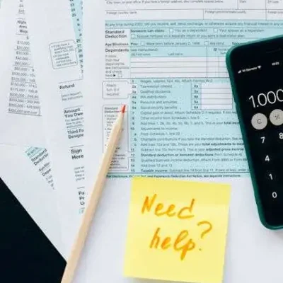 Close-up of tax forms with a calculator and a note asking for assistance.