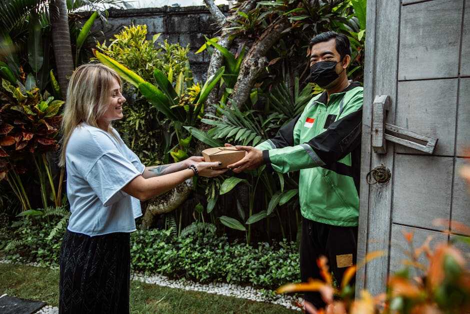 A delivery person hands a package to a woman in a lush garden setting, symbolizing contactless delivery.